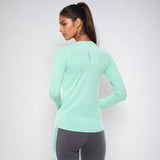 Rear view of a woman wearing the NIVIA Hydra 12 Active Long Sleeve T-Shirt in mint green, showing the back design with full sleeves, paired with grey athletic leggings for fitness and training activities.