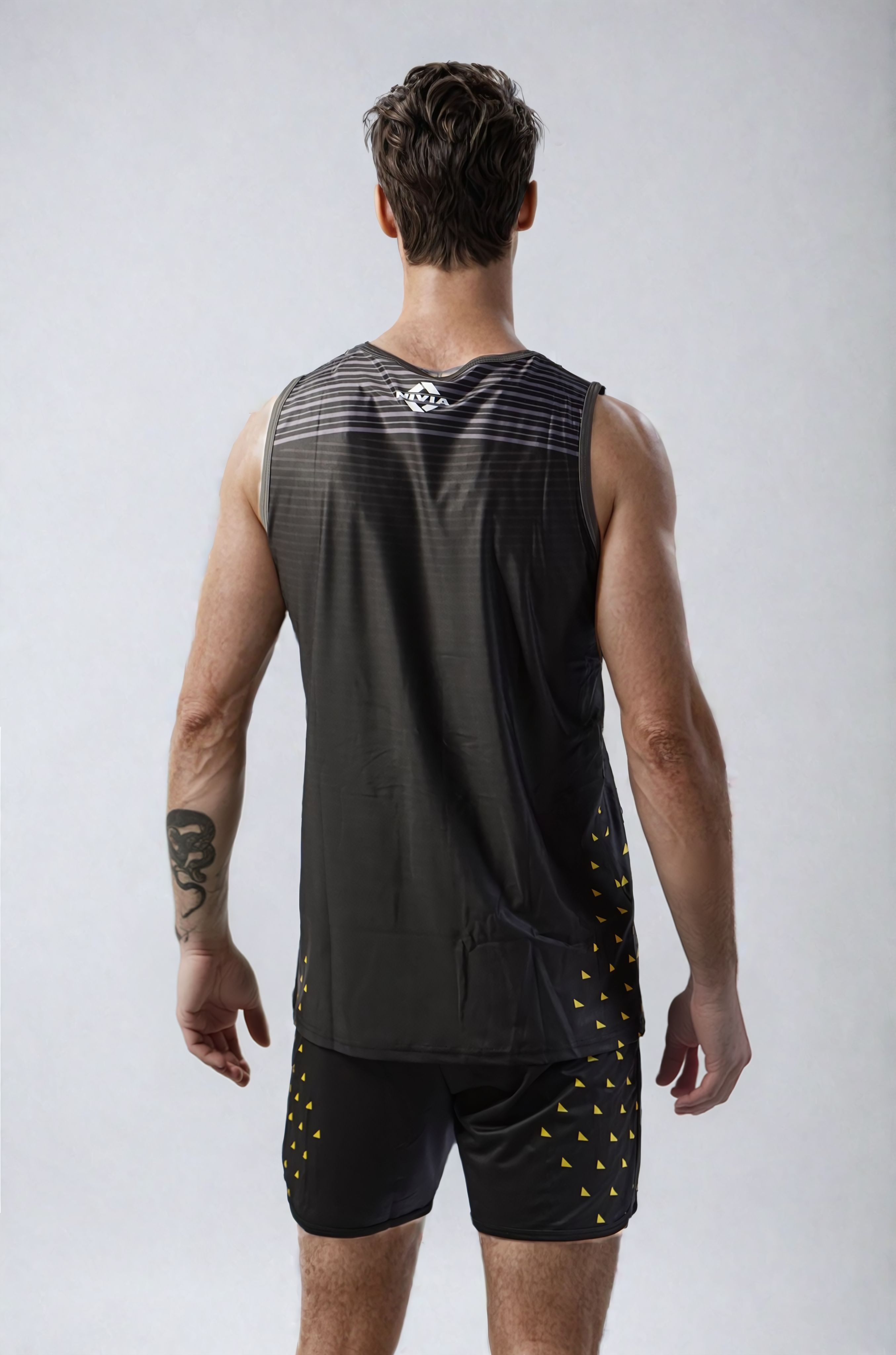 Back view of a model wearing the NIVIA Skylite Track and Field Athletic Kit in black, featuring a sleeveless jersey and matching shorts with yellow accent detailing, suitable for track and field training and sports activities.