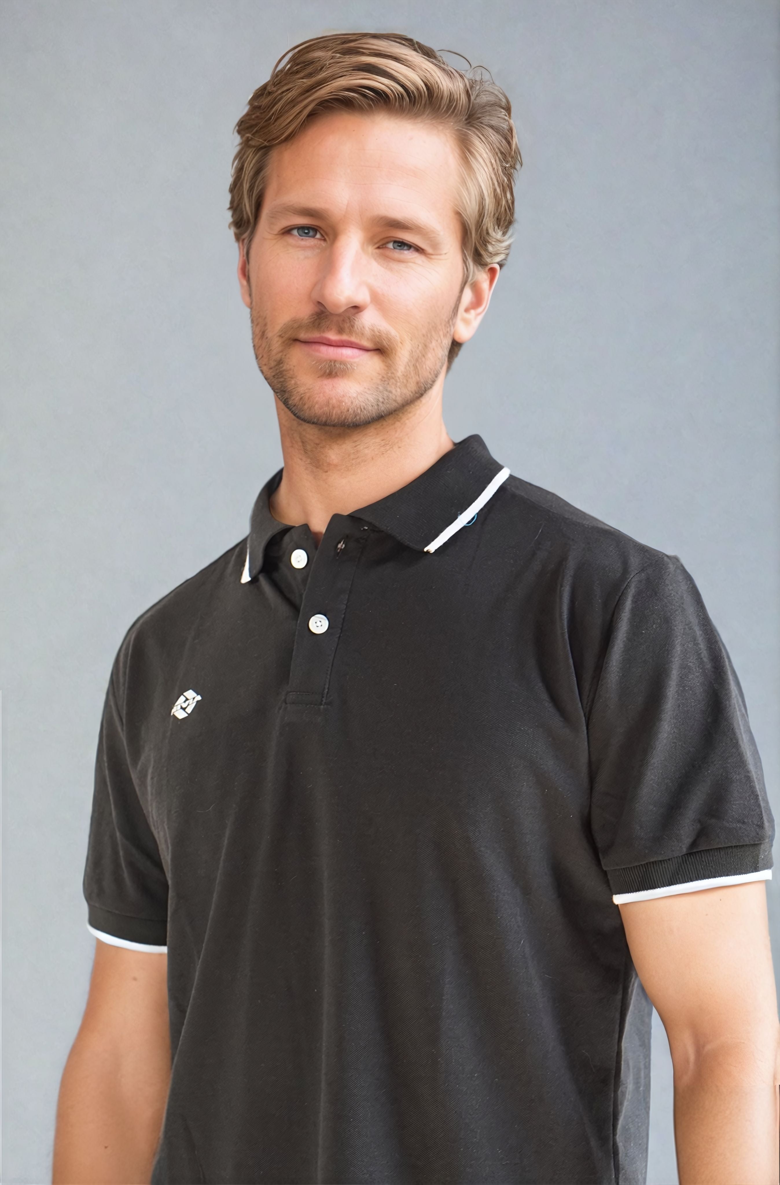 Close-up view of a model wearing the NIVIA Ray 17 Polo Shirt in black, featuring a classic collar with button placket and contrast trim on the collar and sleeve cuffs, made from polyester cotton fabric for casual wear.