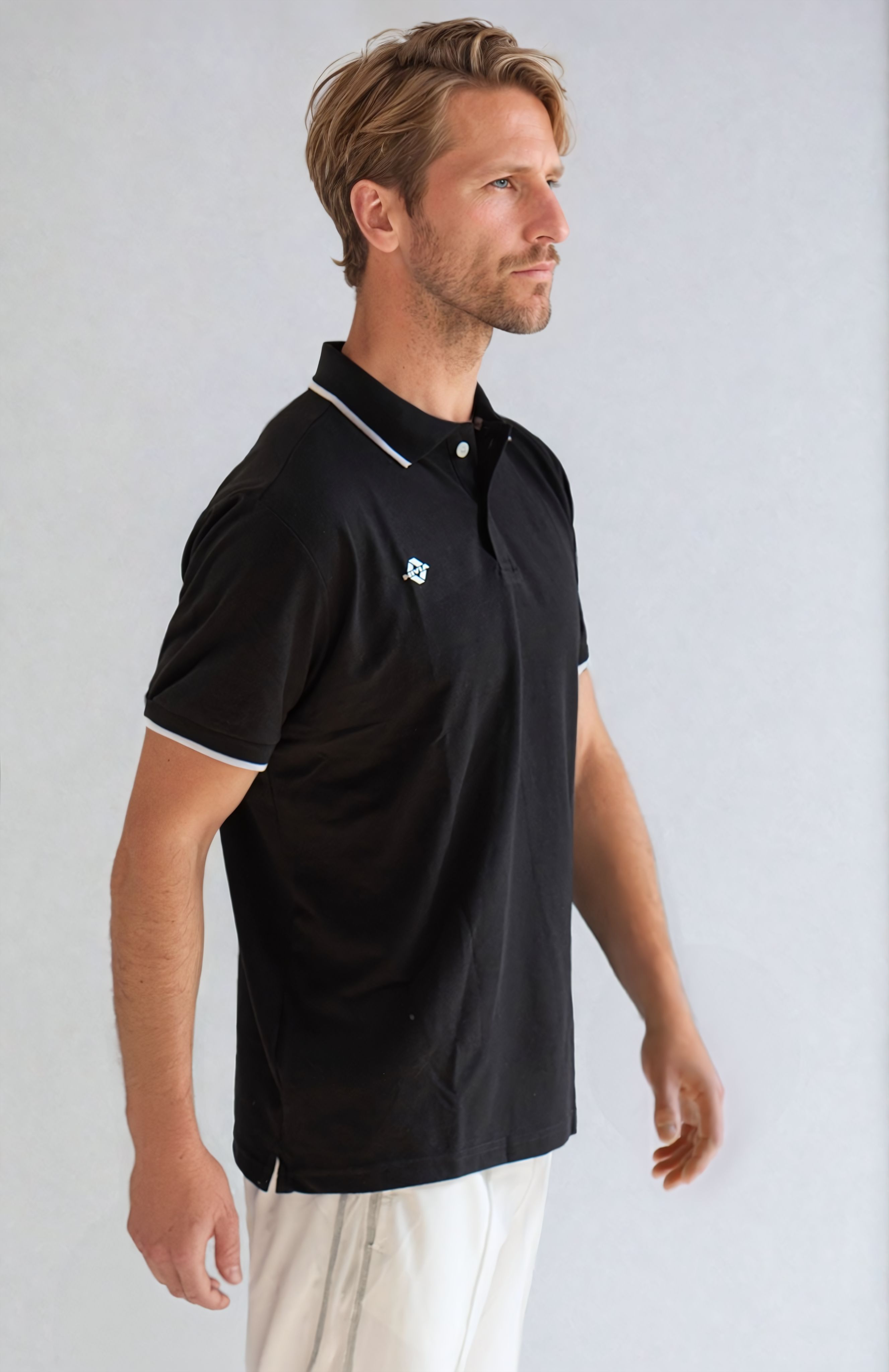 Side view of a model wearing the NIVIA Ray 17 Polo Shirt in black, featuring a classic collar with button placket and contrast trim on the collar and sleeve cuffs, made from polyester cotton fabric for everyday casual wear.