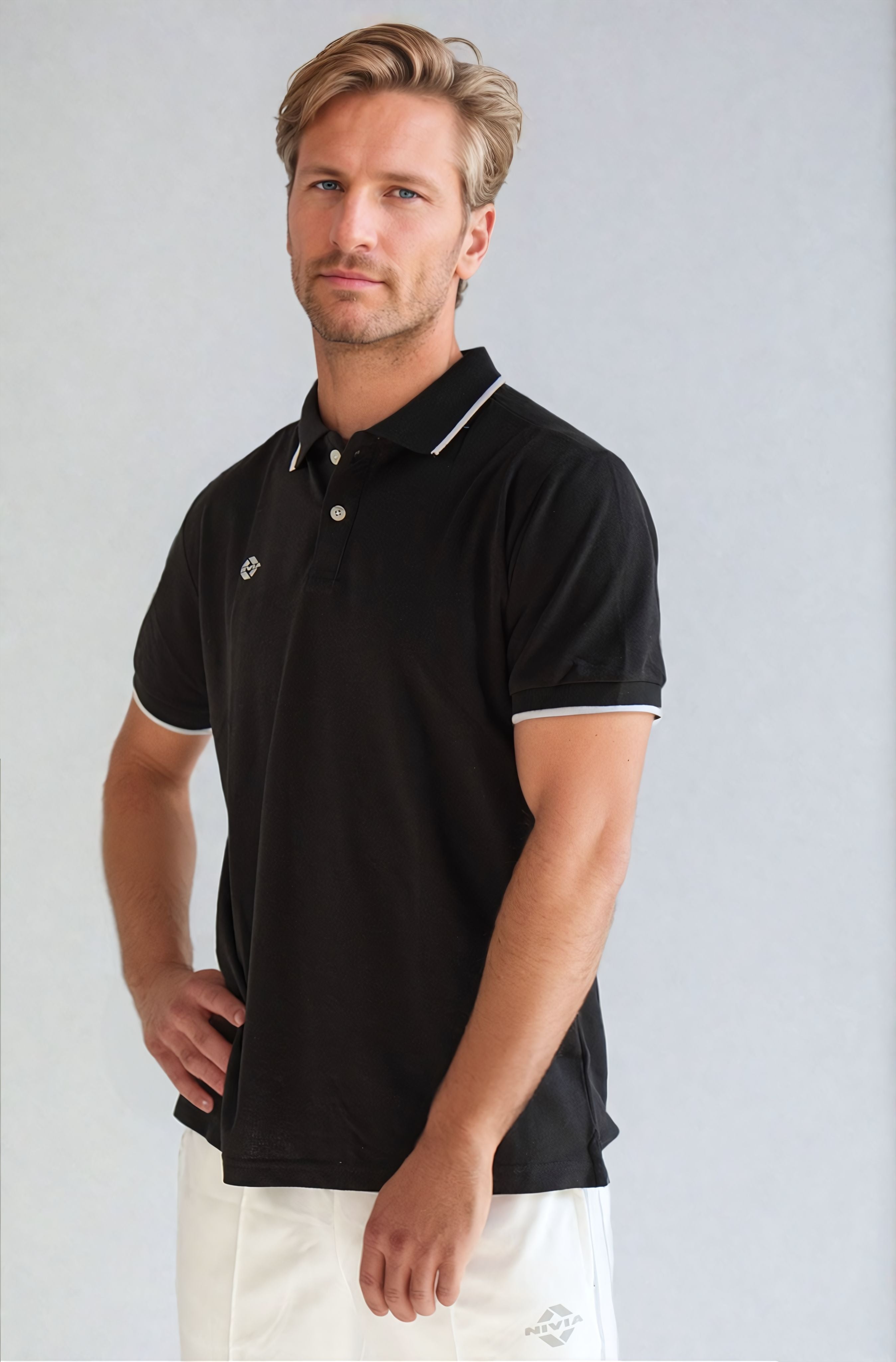Angled front view of a model wearing the NIVIA Ray 17 Polo Shirt in black, featuring a classic collar with button placket and contrast trim on the collar and sleeve cuffs, made from polyester cotton fabric for casual wear.