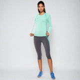 Woman wearing the NIVIA Hydra 12 Active Long Sleeve T-Shirt in a mint green color, paired with grey capri leggings and blue running shoes, styled for fitness and training activities.