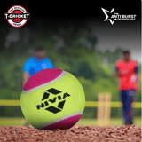 Close-up of a NIVIA Tennis Ball Heavy WT in yellow and pink resting on a cricket pitch, with the NIVIA logo visible, blurred players and stumps in the background, and “T-CRICKET Heavy” and “Anti Burst Technology” icons displayed, highlighting its use for cricket practice and training.