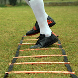 Athlete performing footwork drill on NIVIA Speed Ladder placed on grass, stepping through orange rungs with black side straps during agility training session.