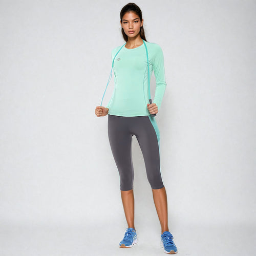 Woman wearing the NIVIA Hydra 12 Active Long Sleeve T-Shirt in a mint green color, paired with grey capri leggings and blue running shoes, styled for fitness and training activities.